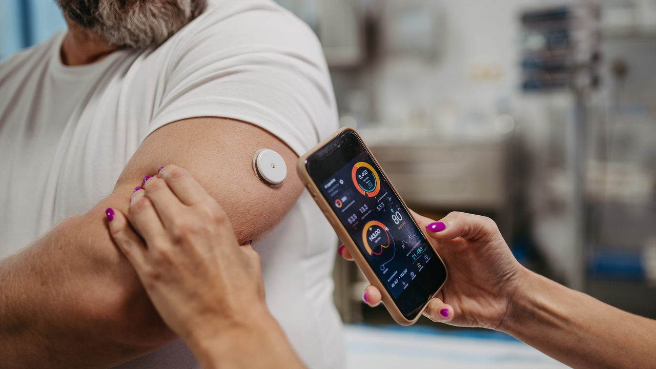 A doctor connecting a continuous glucose monitor with smartphone, to check blood sugar level in real time of an obese, overweight man. Credit: Getty Images
